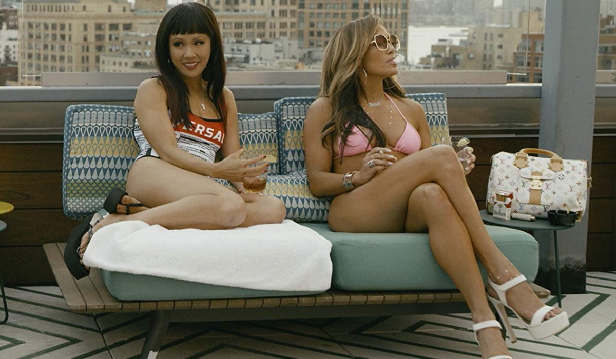 Hustlers Constance Wu and Jennifer Lopez hanging out on a rooftop couch