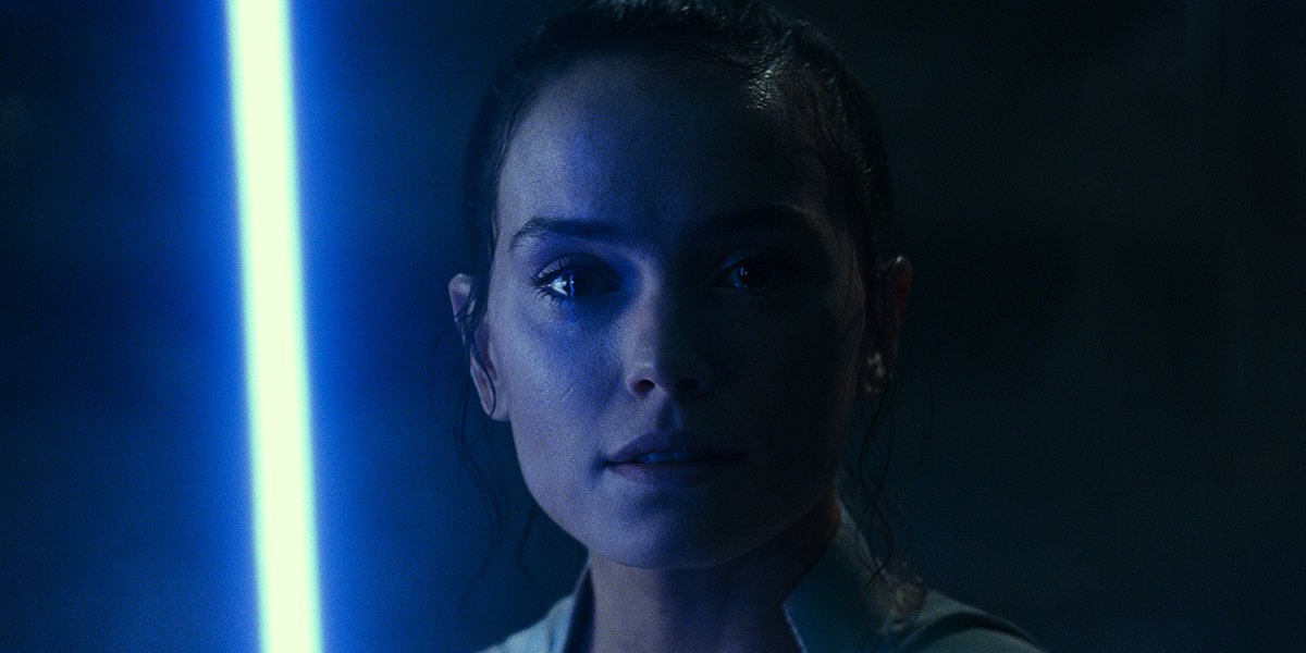 Rey under the blue glow of her lightsaber