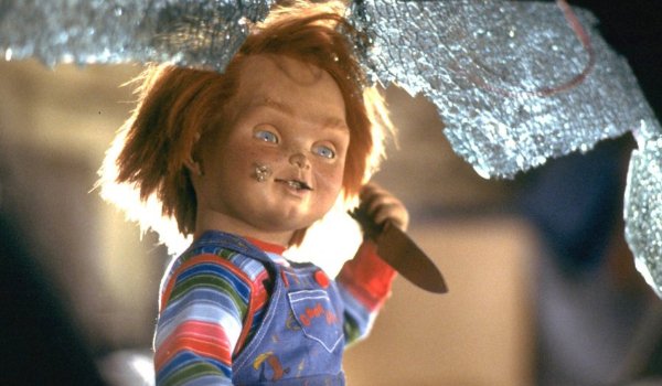 Child's Play Chucky holds a knife framed by a shattered window