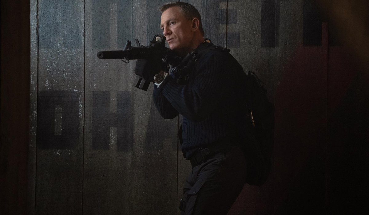 Daniel Craig takes careful aim in a shadowy room in No Time To Die.