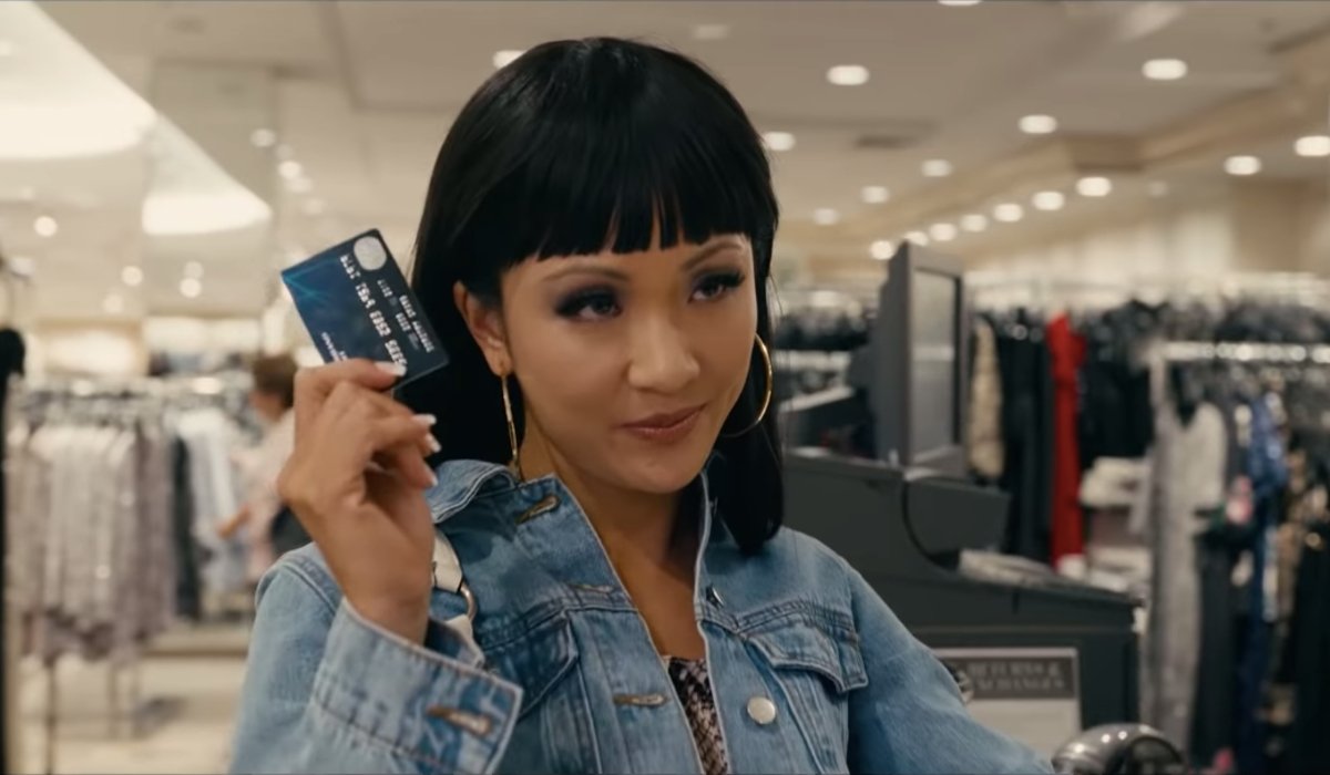 Hustlers Constance Wu flashing a credit card at the mall, with a smile